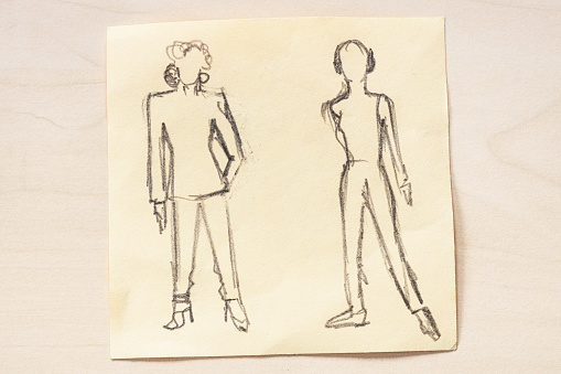 sketch of fashionable silhouette of women of the 80s and the 90s of the XX century hand drawn with black graphite pencil on note paper on light brown table