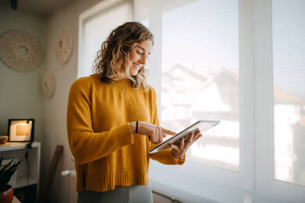 mujer de negocios usando una tableta digital mientras trabaja desde casa - looking at papers fotografías e imágenes de stock