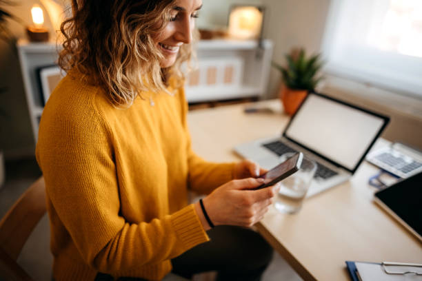 Young woman in a home office Beautiful young woman sitting at the desk in a home office and using a smart phone. business customer engagement stock pictures, royalty-free photos & images