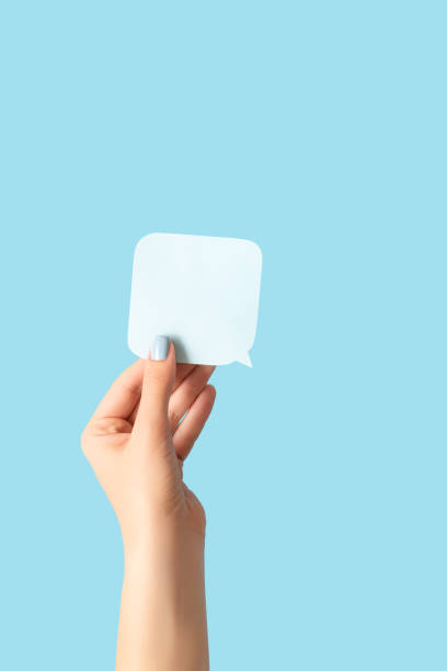 istock Female hand with blue manicure holding a white blank message card. Speech shape banner in female hand on blue background 1348067521