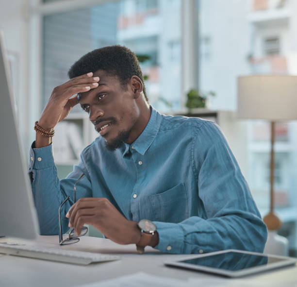 istock Shot of a young businessman looking stressed while using a computer at his desk in a modern office 1348068682