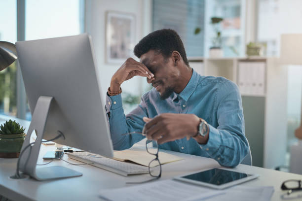 istock Shot of a young businessman looking stressed while using a computer at his desk in a modern office 1348069082