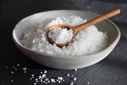 Flower of salt from Guerande - France in a ceramic grey bowl with wooden spoon on a black slate background. Traditional  french natural sea salt of high quality close up.