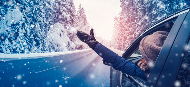 Happy woman in the car on the snowy background. Auto on the winter country road in the forest. Concept of the family vacation and tourism.