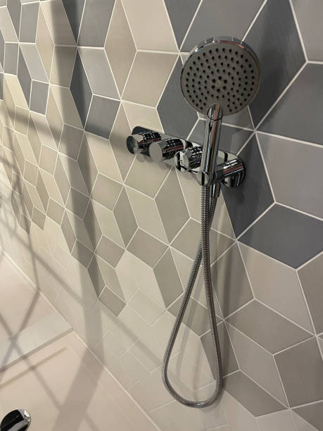 istock Close-up image of modern bathroom with separate shower cubicle, grey, black and white geometric wall tiles in cube pattern design, contemporary chrome shower hanging on wall, drainage hole 1348073251