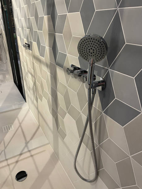 istock Image of modern bathroom with separate shower cubicle, grey, black and white geometric wall tiles in cube pattern design, contemporary chrome shower hanging on wall, drainage hole 1348073264