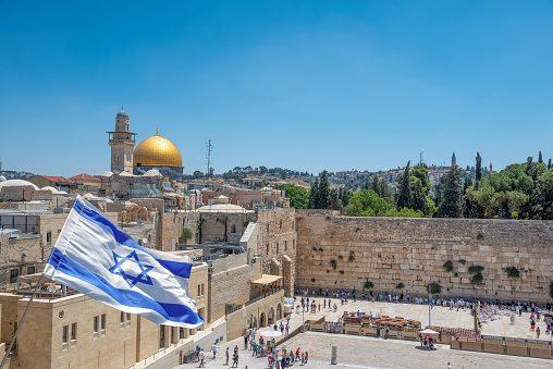Jerusalem, Israel - October 22, 2021; An Israeli flag blows in the wind from an elevated view of the Wailing Wall and the Al-Aqsa Mosque in Jerusalem.