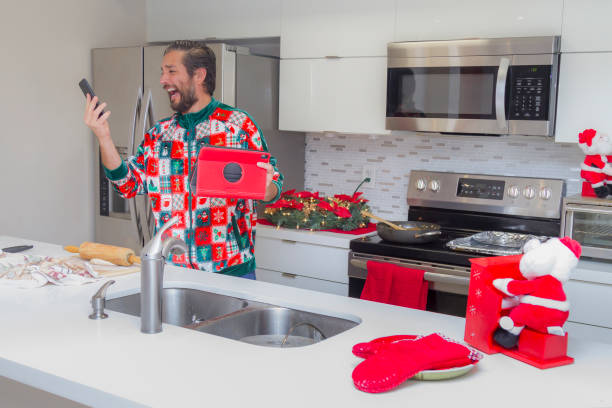 Handsome Latin young man cooking Christmas Dinner / Thanksgiving Dinner for Christmas night / Thanksgiving Day inside in a latin moderm home in Miami, United States wearing a Christmas Shirt / Pajamas Corona Virus Covid-19 Pandemic illness breakdown.
He's having troubles mixing flour for make some christmas cookies following the directions on a video in his Digital Tablet using Wifi and 5G Technology. On back, a nice modern kitchen with christmas decorations / ornaments.
Christmas and New Year celebration traditional treats concept.
People cooking food concept.
Christmas Home Latin Experience in December Holidays Concept.
Thanksgiving Day Concept. joven latino cocinando cena de navidad / cena de acción de gracias para la noche de navidad / día de acción de gracias en el interior de una casa de moda latina en miami, estados unidos con una camisa de navidad / pijama corona virus covid-19 crisis de