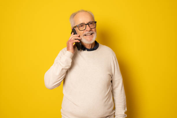 istock Happy senior man using smartphone isolated over yellow background. 1348075136