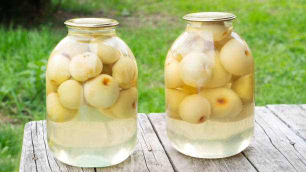 Two glass jars with homemade apple compote. Home preservation from the autumn harvest from the orchard. Pectin from apple compote normalizes bowel function. Homemade apple compote made from fresh organic apples for the winter. Wooden background. Home canning concept. apple compote stock pictures, royalty-free photos & images