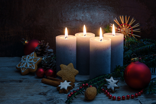 Four Advent candles with Christmas decoration, baubles and cookies on rustic wooden planks against a dark blue background with copy space, selected focus, narrow depth of field
