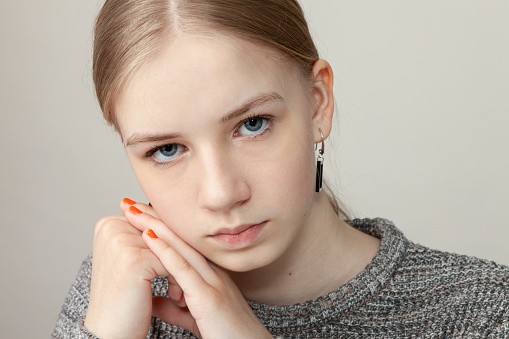 Close up studio portrait of 14 year old blonde teenager girl in gray sweater on gray background