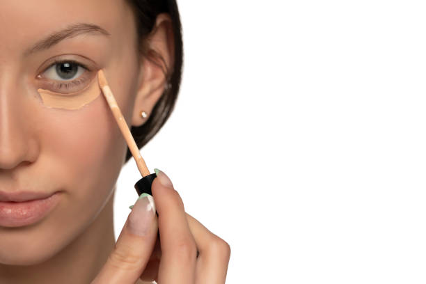 Closeup of young woman with blue eyes applying concealer under her eye Closeup of young woman with blue eyes applying concealer under her eye on a white background concealer stock pictures, royalty-free photos & images