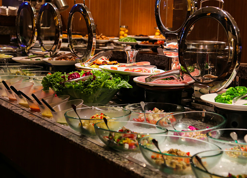 Salad bar with stainless steel tongs in round chafer server and glass bowls at bbq restaurant