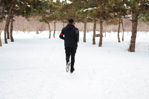 istock Young man running on snow covered winter road in forest 1348100186