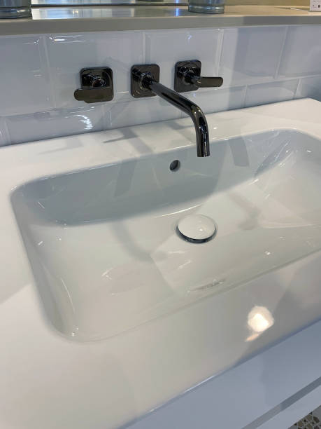 istock Close-up image of black chrome, wall mounted mixer tap over large, white ceramic rectangular sink, luxury bathroom suite 1348100265