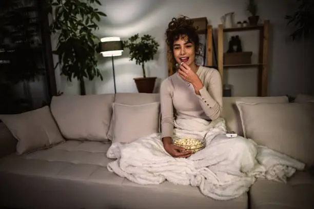 Photo of young  woman eating popcorn and watches movie at home in the evening.