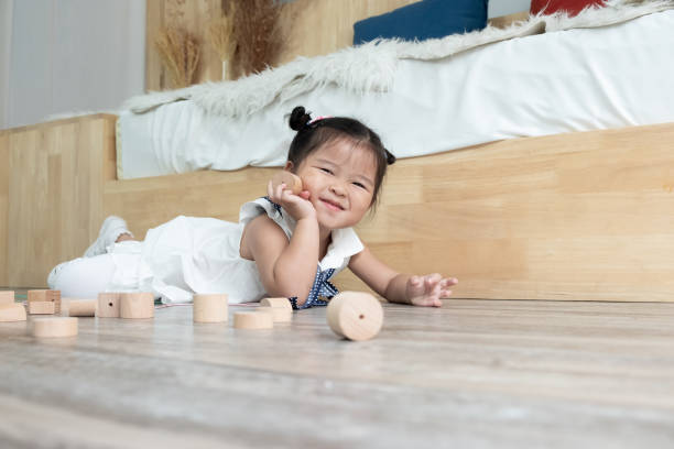 ein kleines asiatisches mädchen legt sich mit holzblockspielzeug auf den boden - child asian ethnicity little girls toddler stock-fotos und bilder