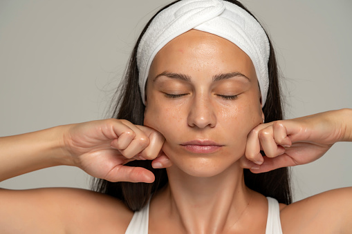 a young woman massaging her face on a gray background