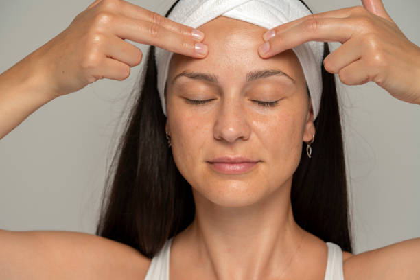una giovane donna con gli occhi chiusi che si massaggia il viso - self massage foto e immagini stock