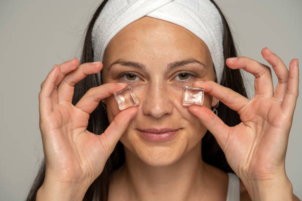 portrait of a young woman holding ice cubes under her eyes stock photo