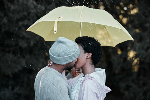 Shot of a young couple kissing while standing under an umbrella