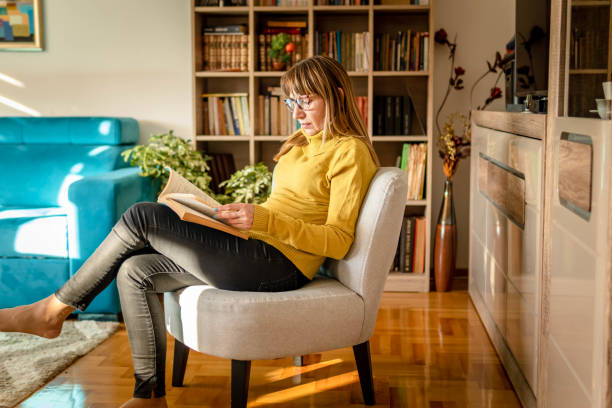 istock Mature woman reading book at home 1348108678