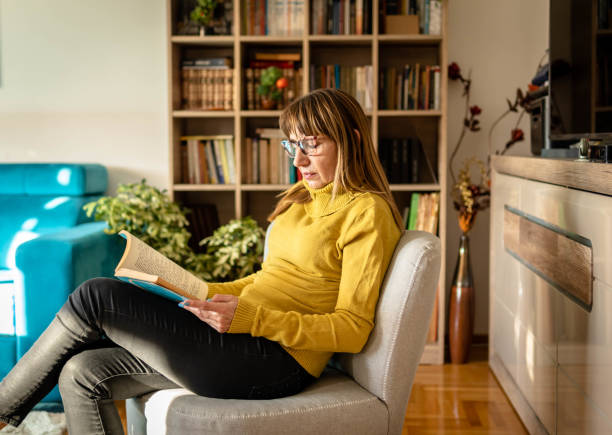 istock Mature woman reading book at home 1348108711