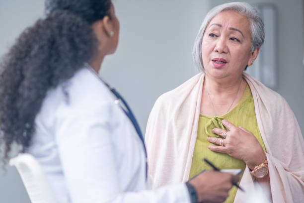 Senior Patient Complaining of Chest Pain A senior woman shares her chest pain symptoms with her doctor at an appointment.  The woman is dressed casually and holding her chest with her hand as she looks downward with a distraught expression.  The doctor is sitting in front of her listening attentively. chest pain stock pictures, royalty-free photos & images