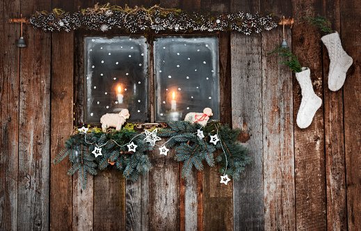 Christmas decoration of wooden walls and Windows in a rustic style. coniferous branches and white socks candlelight through the cozy window. Cheap new year hand made modern minimal style.