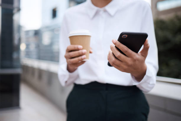 istock Closeup shot of an unrecognisable businesswoman using a cellphone while drinking coffee outside an office 1348122765