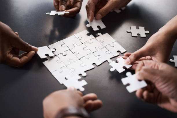primer plano de un grupo de empresarios irreconocibles uniendo piezas del rompecabezas en una oficina - jigsaw puzzle fotografías e imágenes de stock
