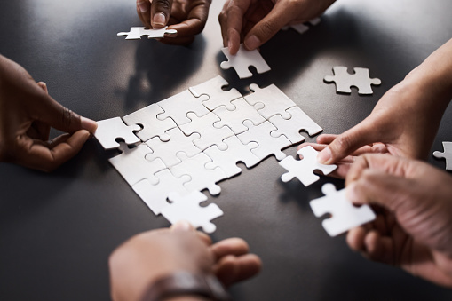 Closeup shot of a group of unrecognisable businesspeople joining puzzle pieces together in an office