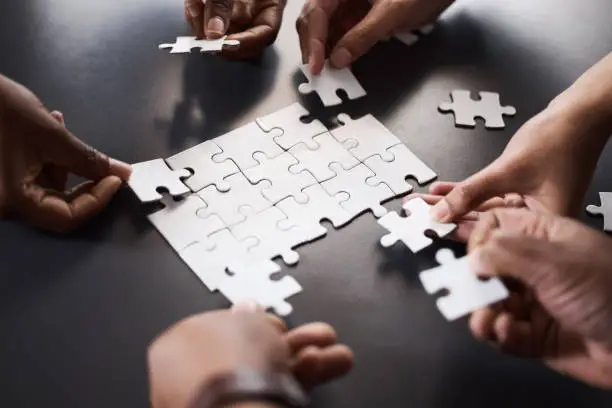 Photo of Closeup shot of a group of unrecognisable businesspeople joining puzzle pieces together in an office