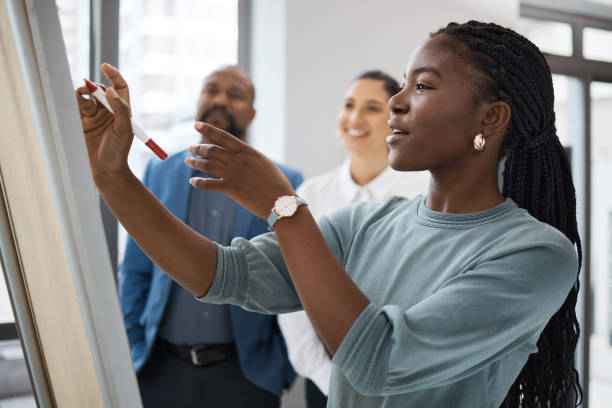 scatto di una giovane imprenditrice che usa una lavagna mentre fa brainstorming con i suoi colleghi in un ufficio - spremersi le meningi foto e immagini stock