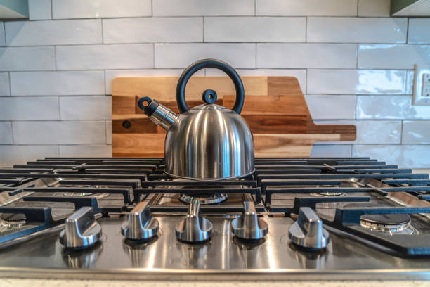 istock Kettle on top of the burner of a cooktop with five knobs on the control panel 1348123664