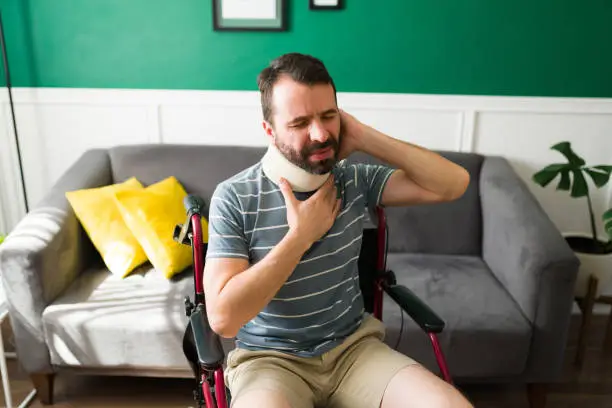 Sad man had a bad accident and wearing a cervical collar. Latin man suffering and in pain while sitting in a wheelchair