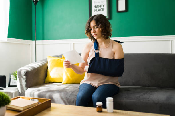 attractive woman taking medicine after an accident - arm sling imagens e fotografias de stock