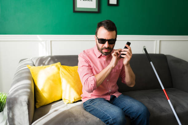 Latin disabled man sending a text Smart blind man texting on his smartphone. Attractive man with a disability using his phone while sitting on the couch blindness stock pictures, royalty-free photos & images