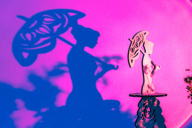 Tender small statue of young woman holding sun umbrella casting dark shadow on purple surface illuminated by bright spotlight beam