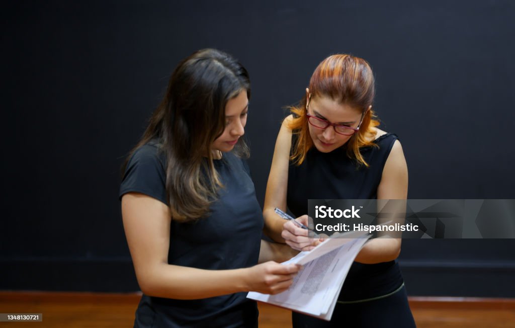 Drama teacher helping a student with her script in an acting class Latin American drama teacher helping a student with her script in an acting class - performing arts concepts Film Script Stock Photo
