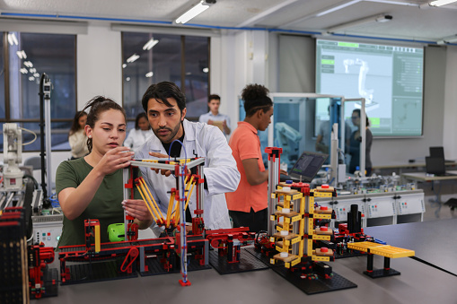 Teacher helping a female student in a robotics class at the university while building a project - STEM education concepts