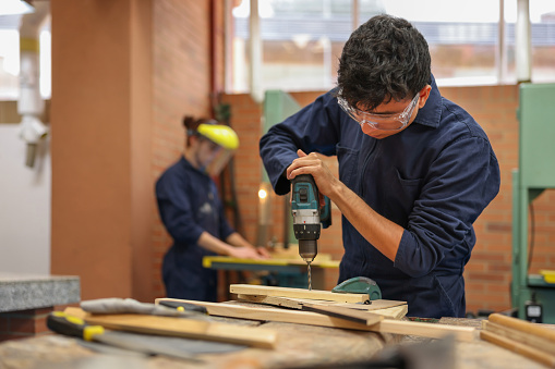 Latin American College student drilling on wood in carpentry class while building a piece of furniture
