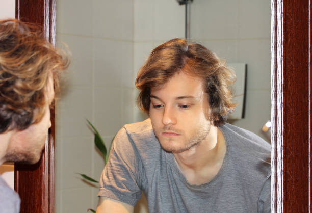 istock young man looking in the mirror,combing his hair,looking at problems on face 1348131827