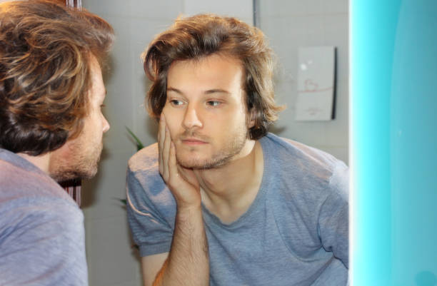 istock young man looking in the mirror,combing his hair,looking at problems on face 1348131830