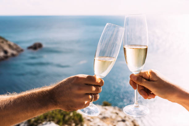 Hands holding champagne glasses over the sea. Romantic vacation. Two hands holding champagne glasses on the background of the sea. Toast with champagne glasses on the seashore. Copy space stock photo