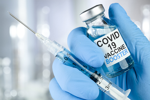 Entregue guantes médicos azules sosteniendo una jeringa y un vial de vacuna con el texto de Covid 19 Vaccine Booster, para la vacuna de refuerzo contra el coronavirus. photo