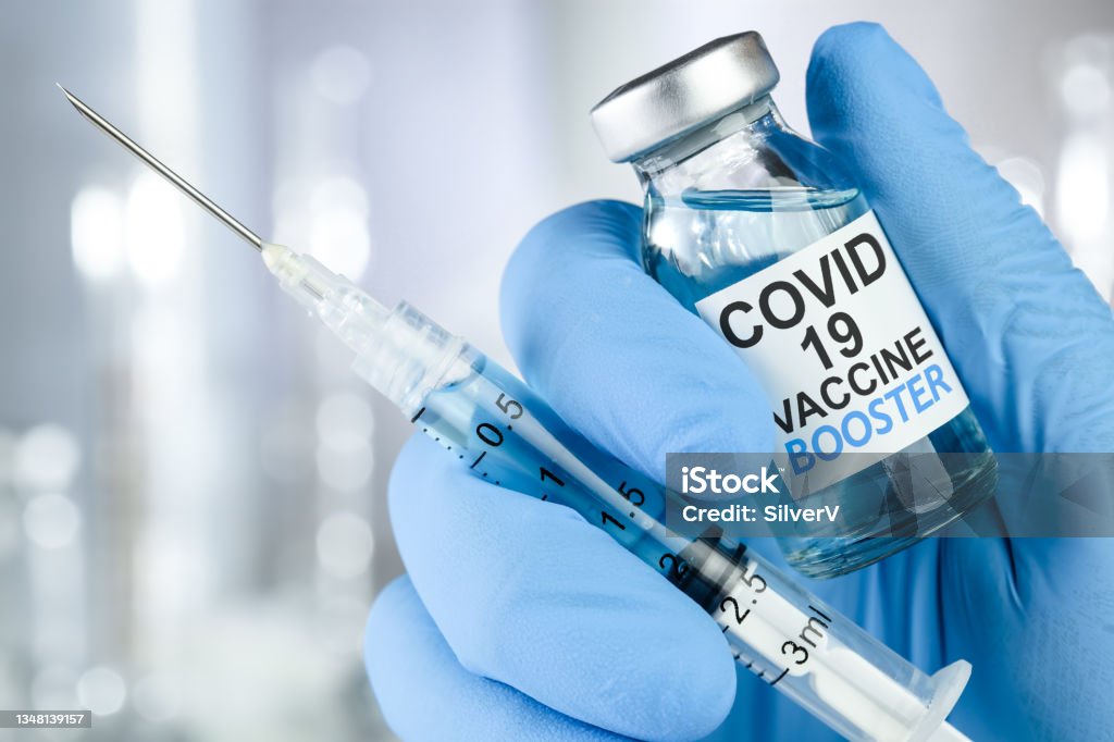 Hand in blue medical gloves holding a syringe and vaccine vial with Covid 19 Vaccine Booster text, for Coronavirus booster shot. Booster Dose Stock Photo