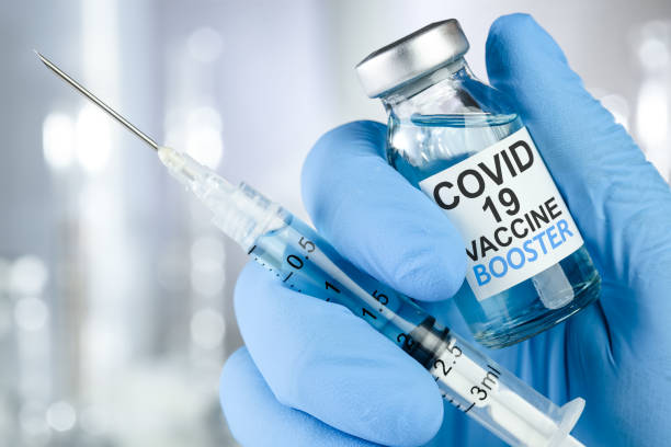 рука в синих медицинских перчатках, держащая шприц и флакон с вакциной с текстом covid 19 vaccine booster, для прививки от коронавируса. - коронавирус стоковые фото и изображения