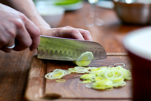 Hands with knife cutting a leek. Ingredients preparation concept.